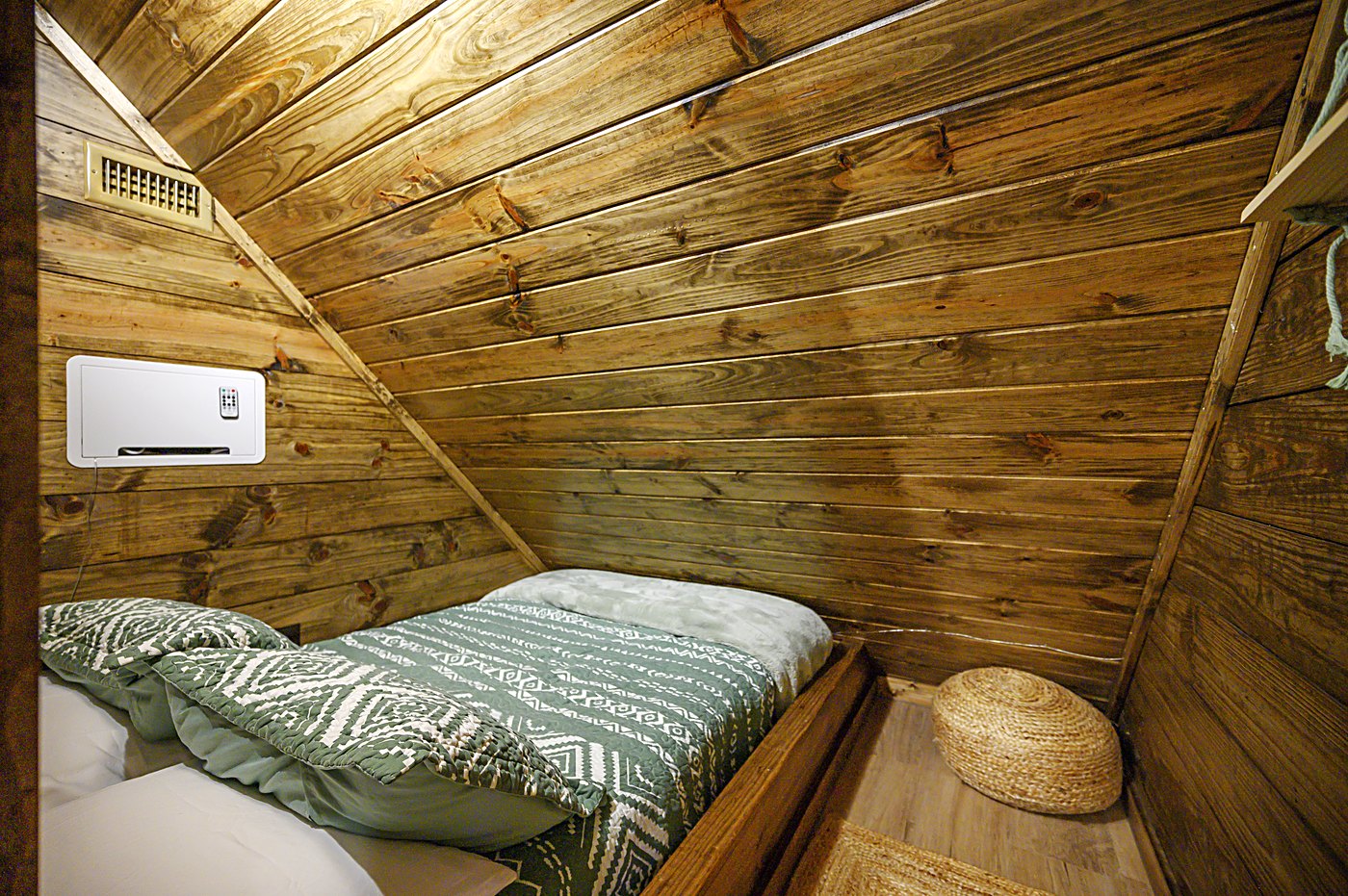 Sleeping nook with a full bed tucked under the sloped pine ceiling